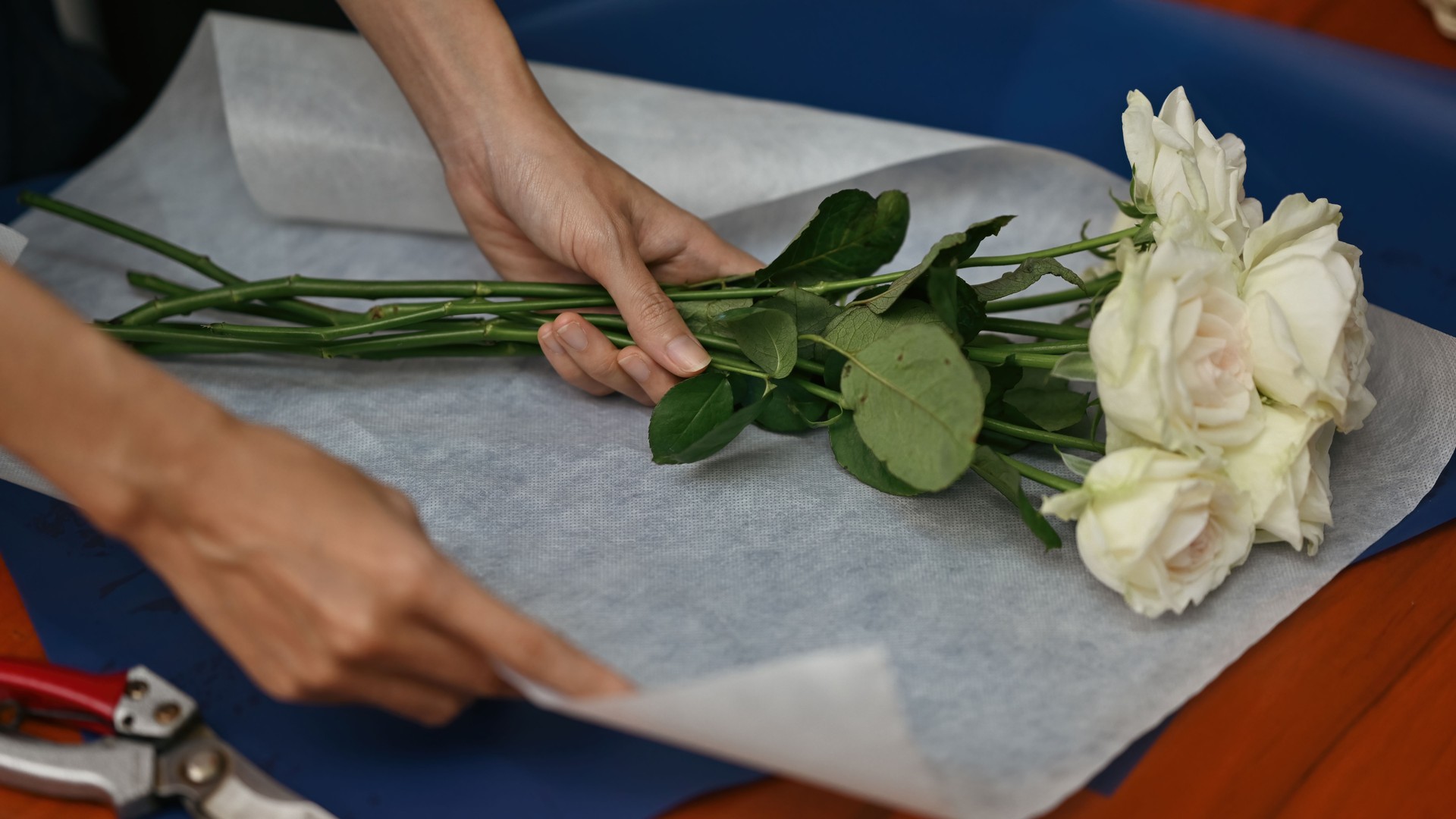 Close-up image of a Hands Wrapping White Roses in Paper for Bouquet